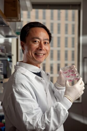 Photo: Su-Chun Zhang in white lab coat and gloves holding a glass container