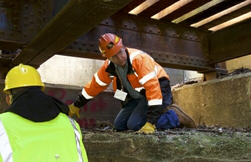 Photo: Man in hardhat under rail ties on bridge