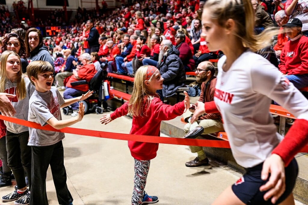 Volleyball team members jog out onto the court and high-five a young fan.