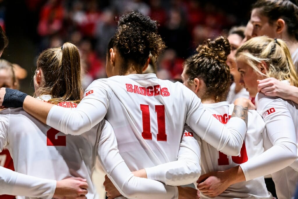 Volleyball team members put their arms around each other to huddle before a game.