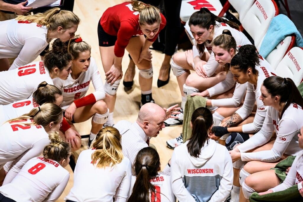 Team members huddle around the coach, who is giving them instructions during a timeout.