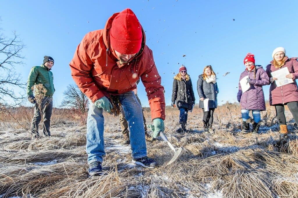 Photo: Man digging with pick while students watch