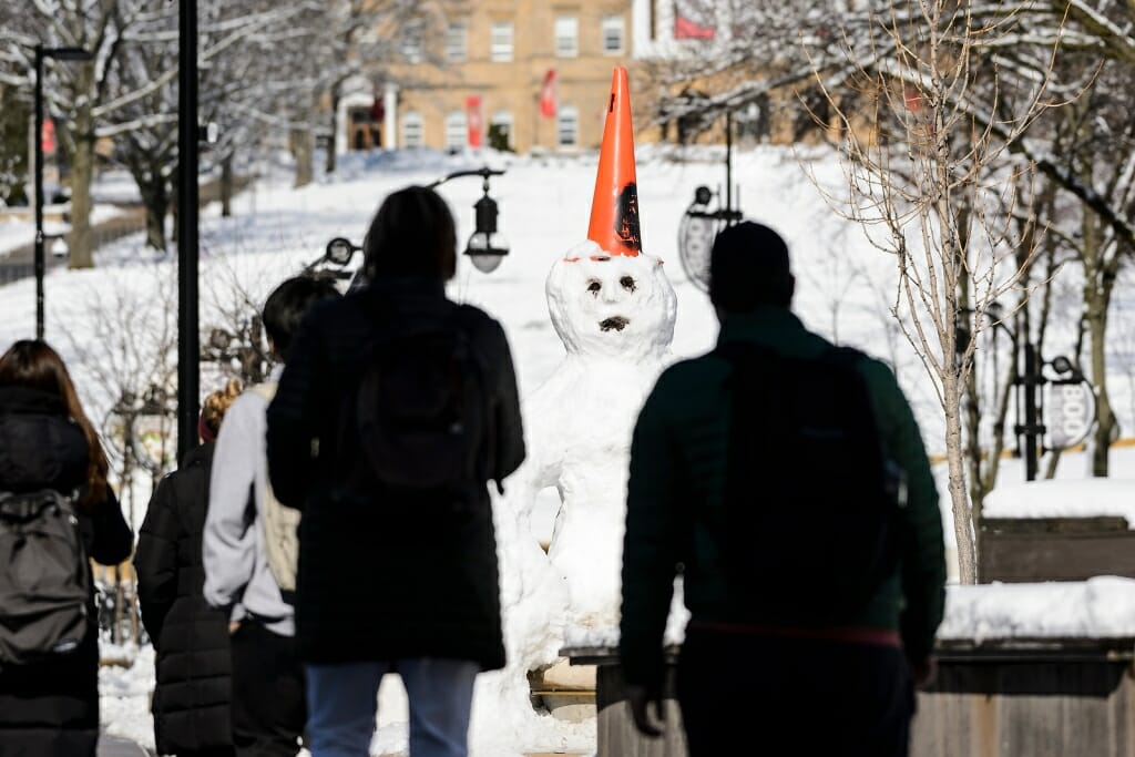 Photo: People looking at snowman with orange construction cone on head