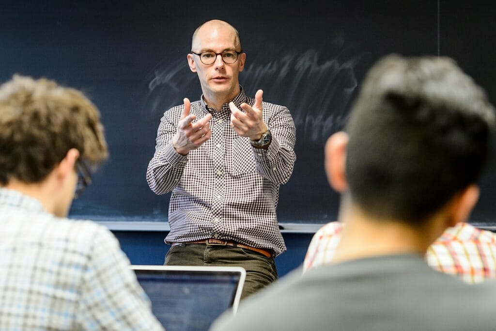 Photo: Camal gesturing to class in front of blackboard