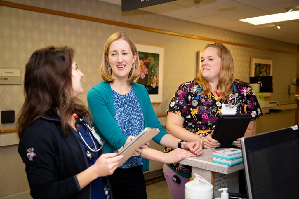 Three women - a researcher and two nurses - talk in a hospital setting.