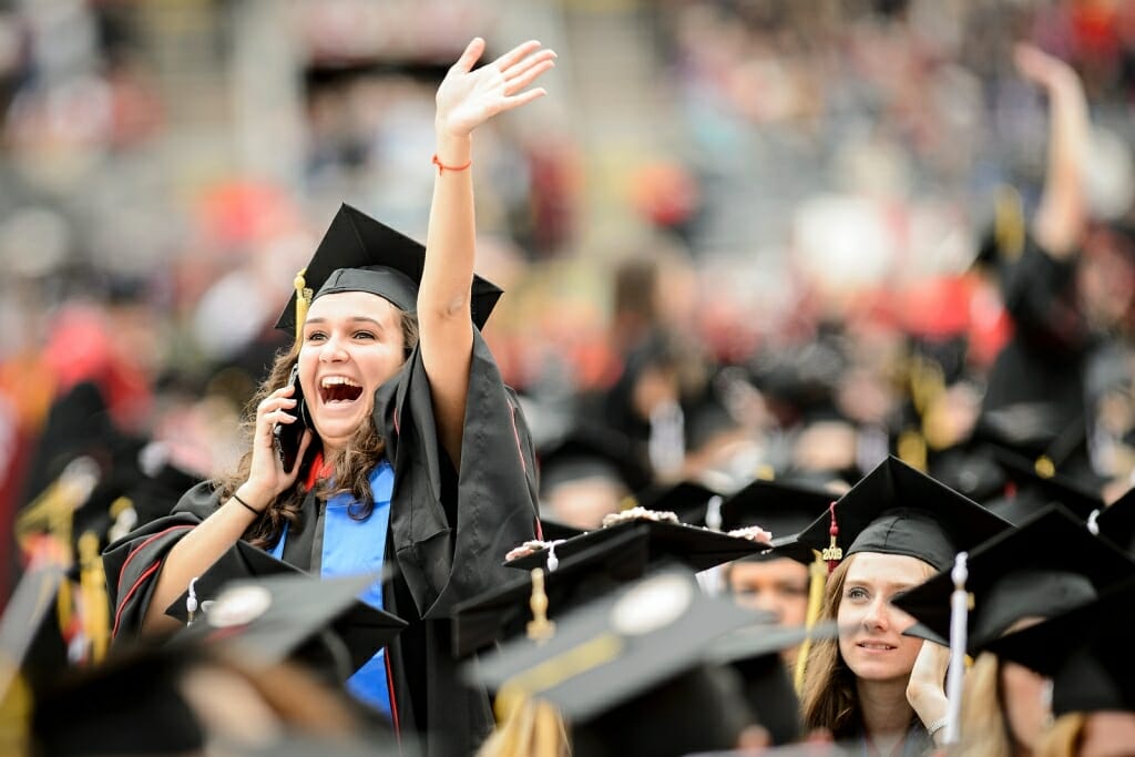 Photo: Student in cap and gown waving and talking on phone