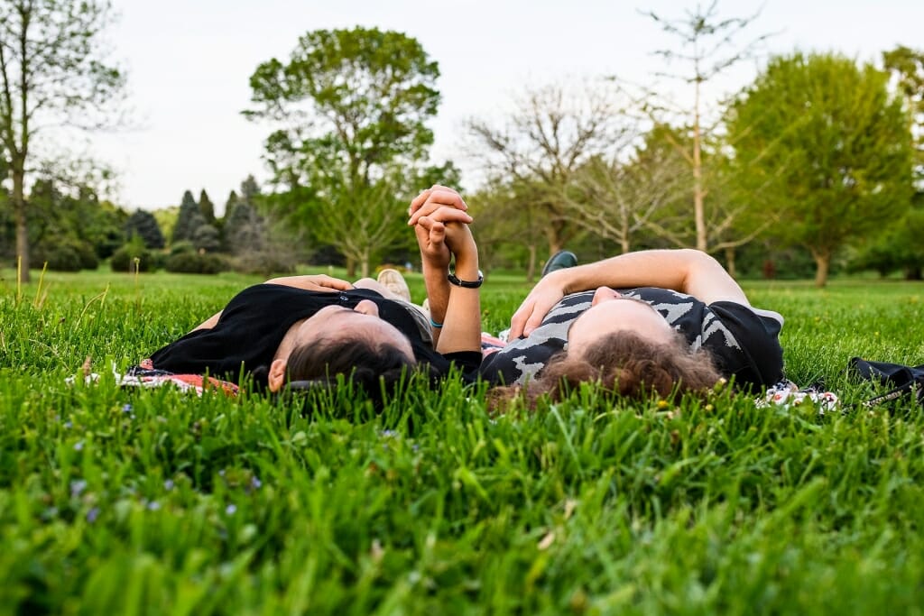 Photo: Two people lying on their backs in the grass, holding hands