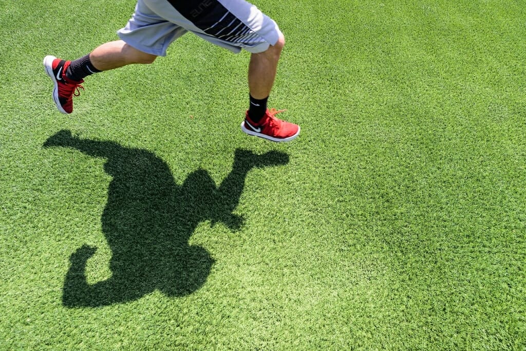 Photo: Closeup of legs of a runner casting shadow on the grass