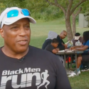 Still frame from video: Aaron Perry outside in front of a picnic table with young people sitting at it