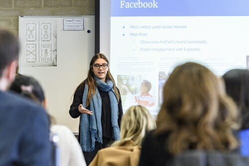 Photo: A student presenting to a classroom of people, with a slide on the overhead.