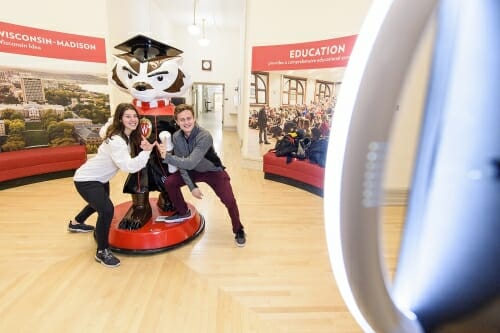 Two people post in front of a Bucky Badger statue. They flash the W.