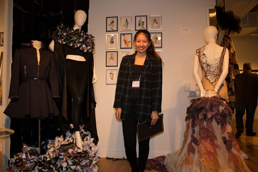 A photo of a woman with the dresses she designed.