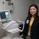 Photo of a woman next to a teleopththalmology machine. She's smiling.