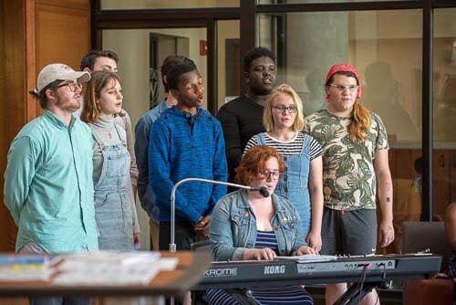 Photo: Students gather around a keyboard while a woman sings.