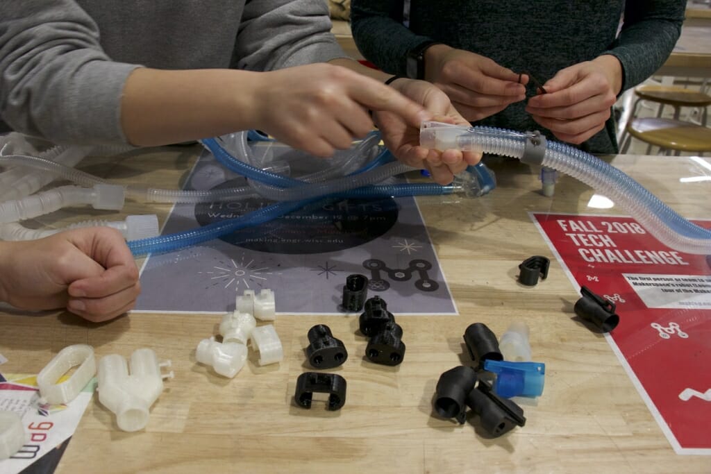 Three sets of hands work on plastic tubing.