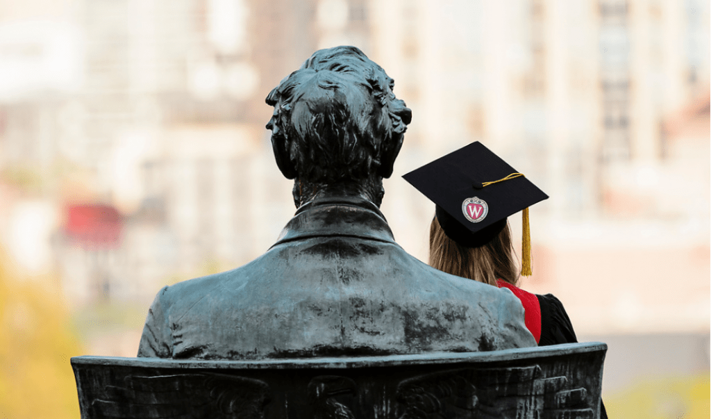 A soon-to-be graduate sits in the lap of the Abraham Lincoln statue on Bascom Hill.