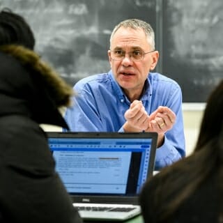 Photo: Ediger seated and gesturing to seated student with laptop