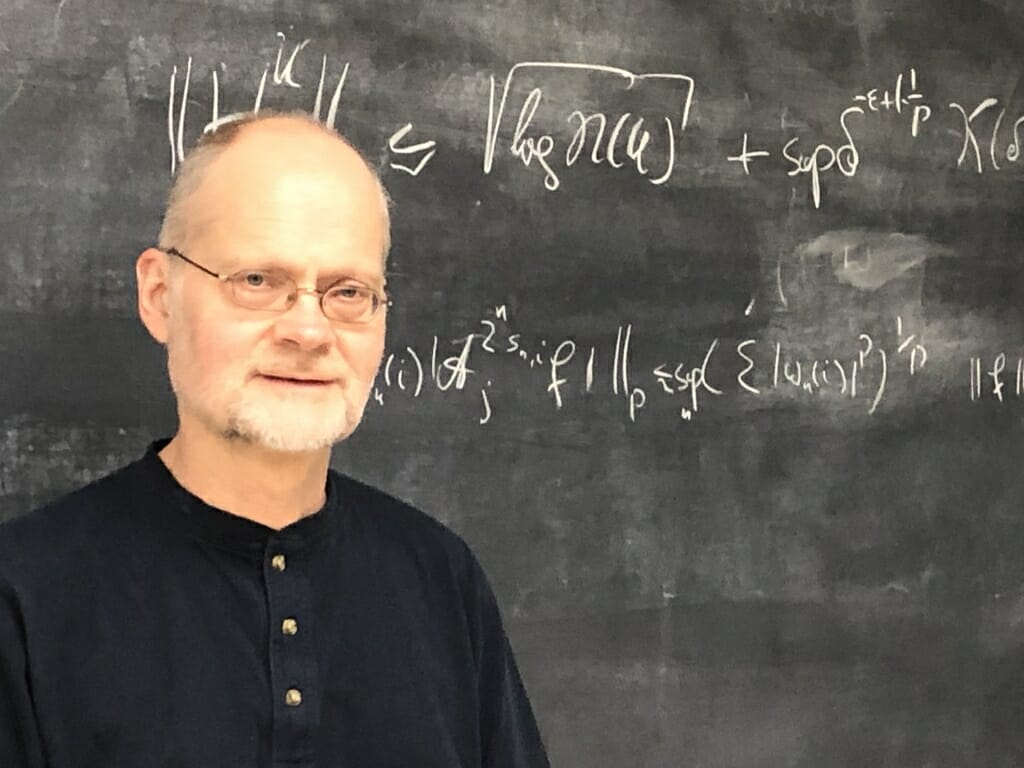 Photo: Andreas Seeger standing in front of a chalkboard with equation on it