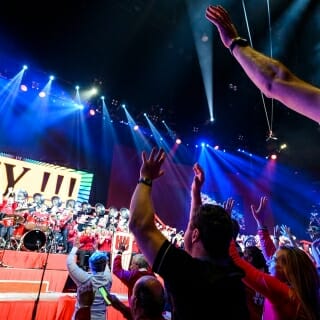 Photo: Under the lights, audience members raise their hands and dance.