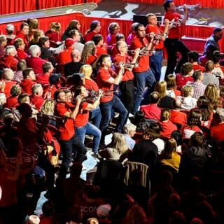 Photo: Former band members wearing red playing their instruments in the aisle.