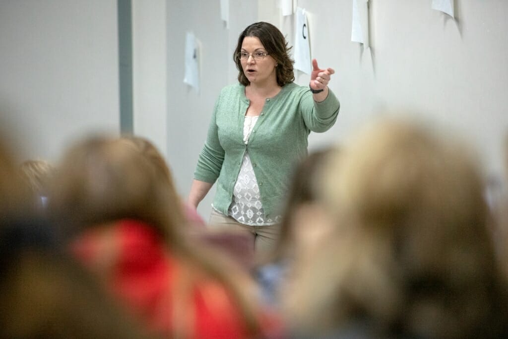 Photo: A woman gesticulates as she speaks to a group of students.