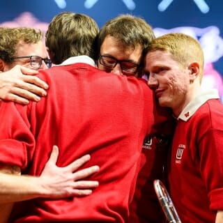 Photo: Band members wearing red sweaters hug.