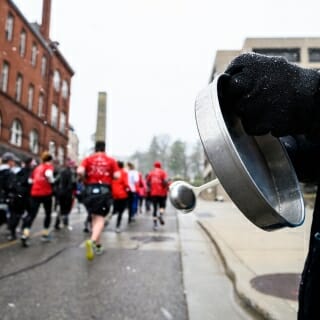 Photo: A volunteer hits a drum with a runners in the background.