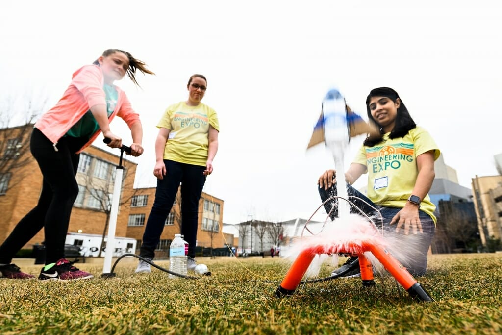 Photo of a child launching a water rocket with help from two students.