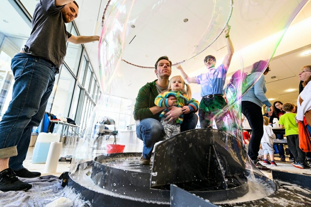 Photo: Father with daughter on lap blow bubbles.