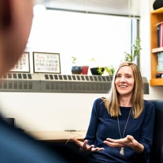 Photo: Abbey sitting in front of whiteboard talking to unidentified person