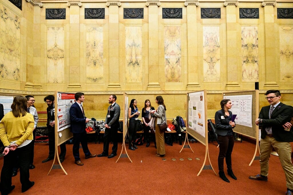 Photo: People standing and conversing in ornate marble hearing room