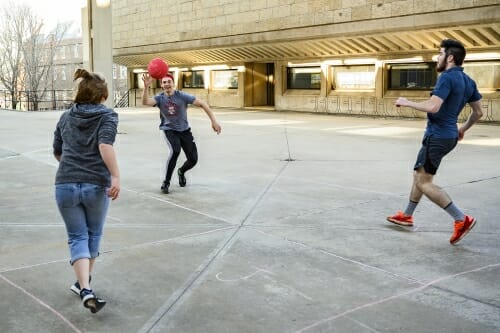 Photo: Three students play with a ball on a concrete surface.