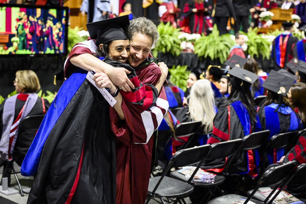 Photo of a new graduate being hugged by a professor.