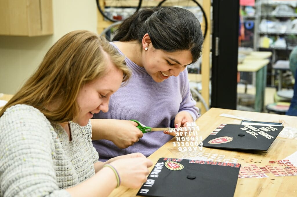 Photo: Two women put white letterrs on their black mortarboard caps.