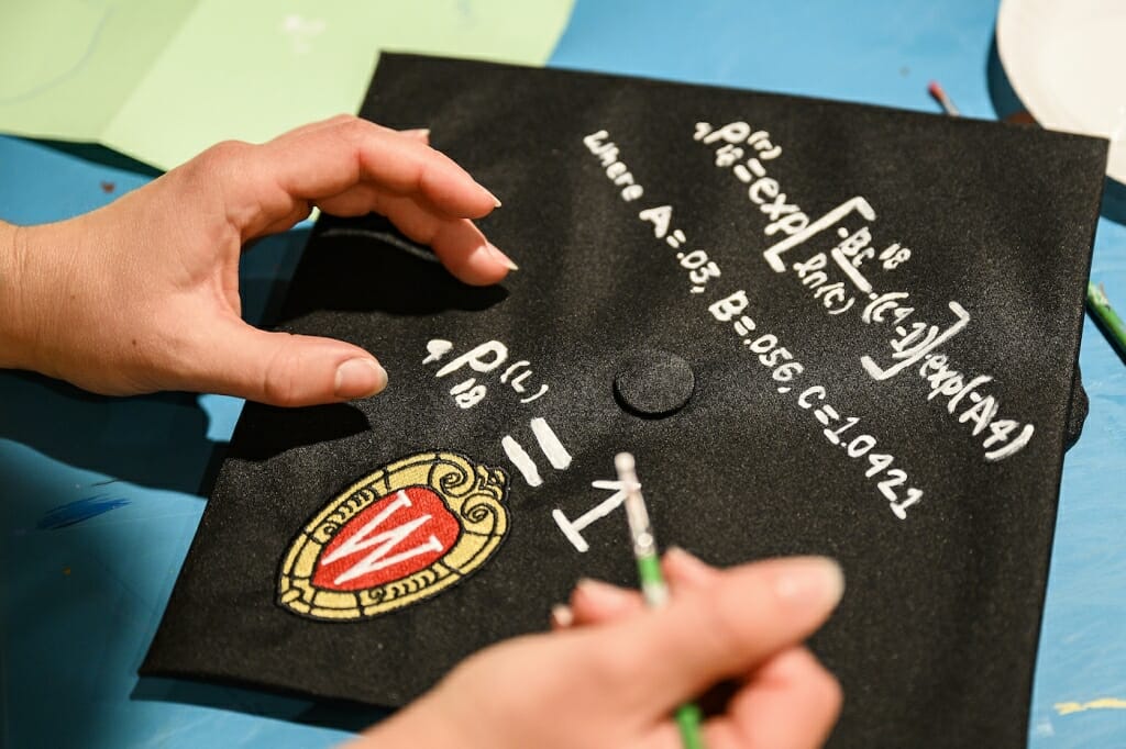 Photo: A hand paints a complex equation in white on a black cap.