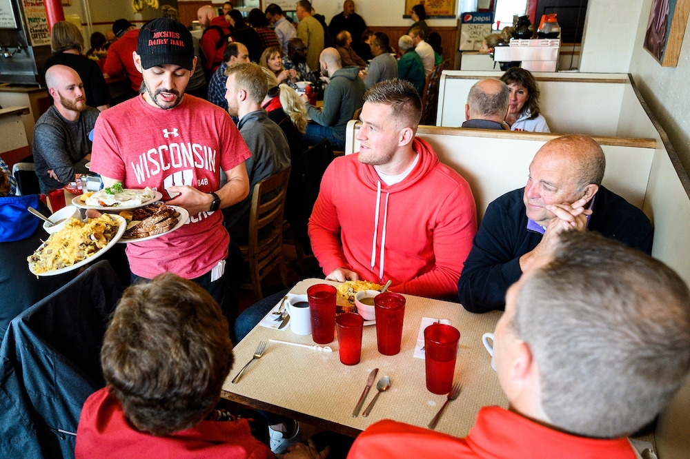 Photo of a waiter delivering plates of food to the table where speaker J.J. Watt and others are seated.