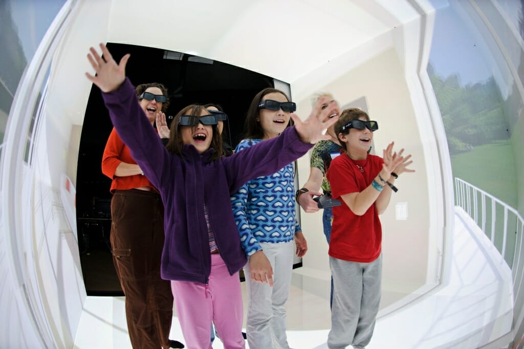 Wearing 3-D eyeglasses and holding a virtual-reality controller, visitors step through a room-sized, computer-generated version of a living room patio door and interact their surroundings during a Living Environments Laboratory Open House at the Wisconsin Institutes for Discovery (WID) at the University of Wisconsin–Madison on Nov. 5, 2011. The room consists of a Cave Automatic Virtual Environment (CAVE), where scientists can re-create a place, observe how someone might use personal-care technology and make related changes earlier in a product's development process. The lab is led by Patricia Flatley Brennan and is part of the publicly funded Wisconsin Institute for Discovery. (Photo by Jeff Miller/UW-Madison)