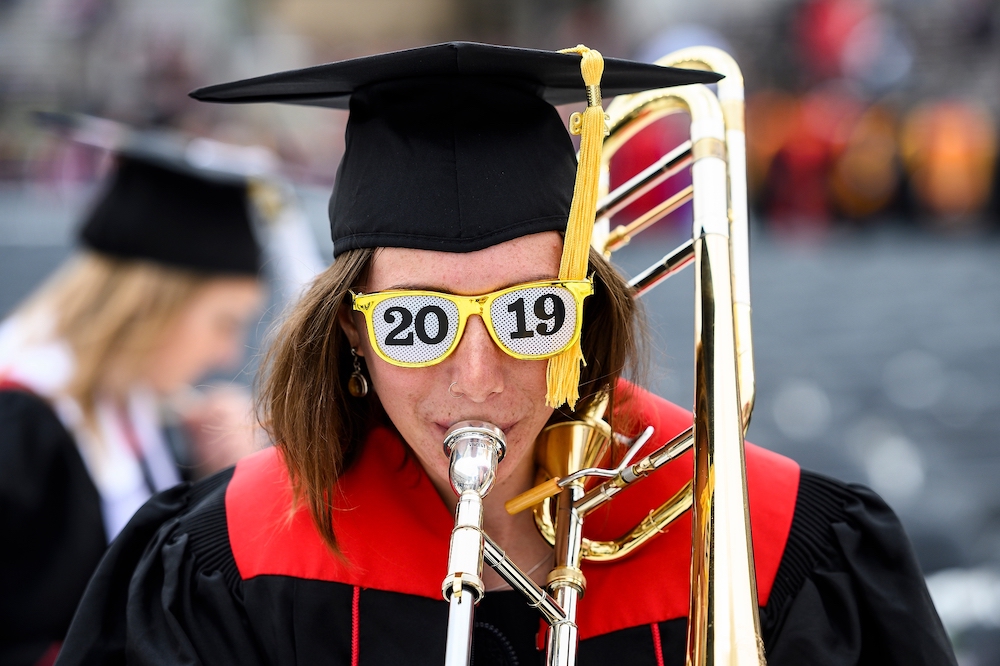 Photo of a graduate playing the trumpet and wearing sunglasses that read '2019.'