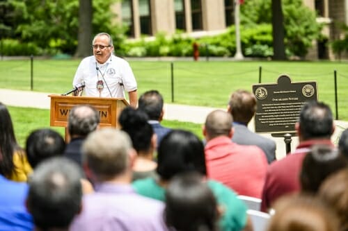 Photo: Cleveland speaking outdoors at podium next to plaque