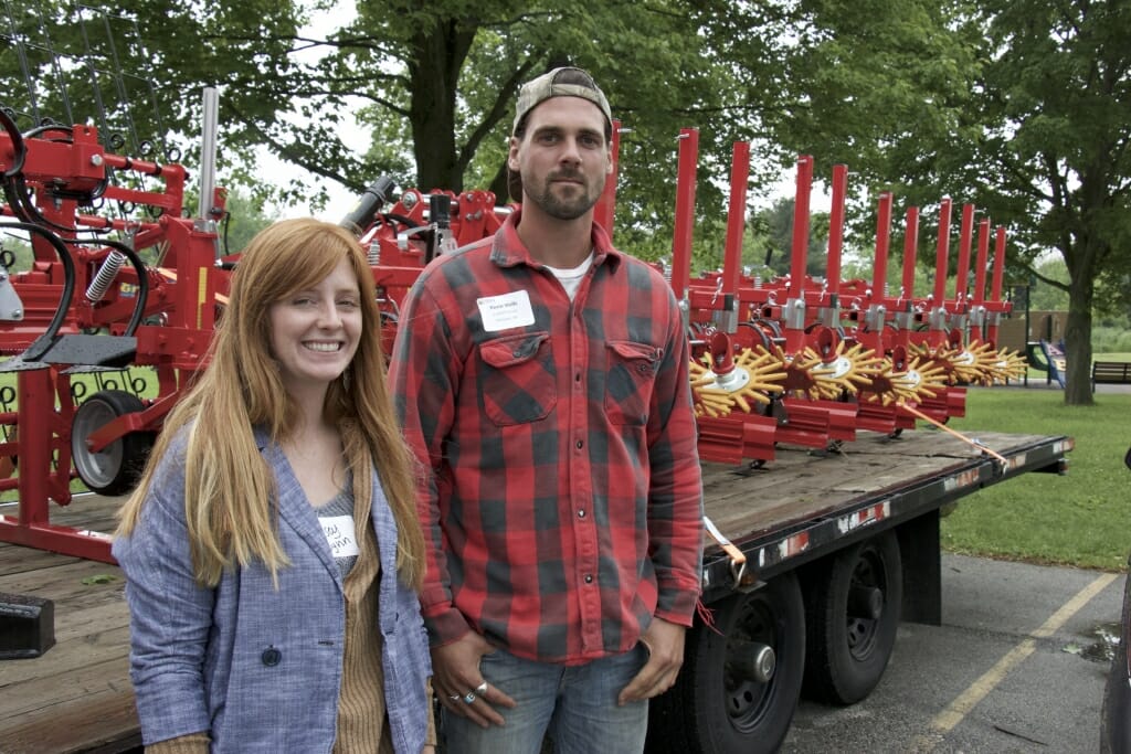 A man and a woman stand in front of some farm equipment.