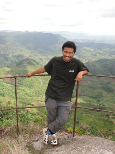 Photo: A man stands in front of a forested landscape.