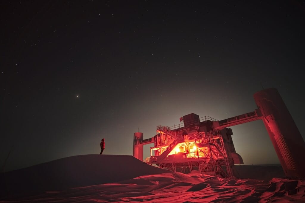 Photo: Reddish-lit exterior of observatory at night backlit by bright moon