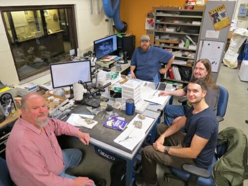 Photo a group of researchers gather around a desk.