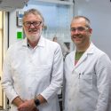 Photo; Two men in white lab coats smile in a lab.