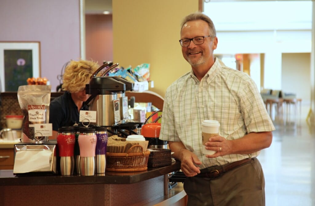 Photo: Mike Sanders leans on a desk and drinks coffee.