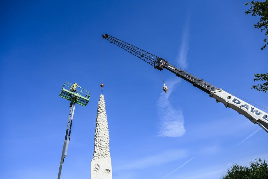 Photo: A worker on a lift next to the statue, ties a wire to it.