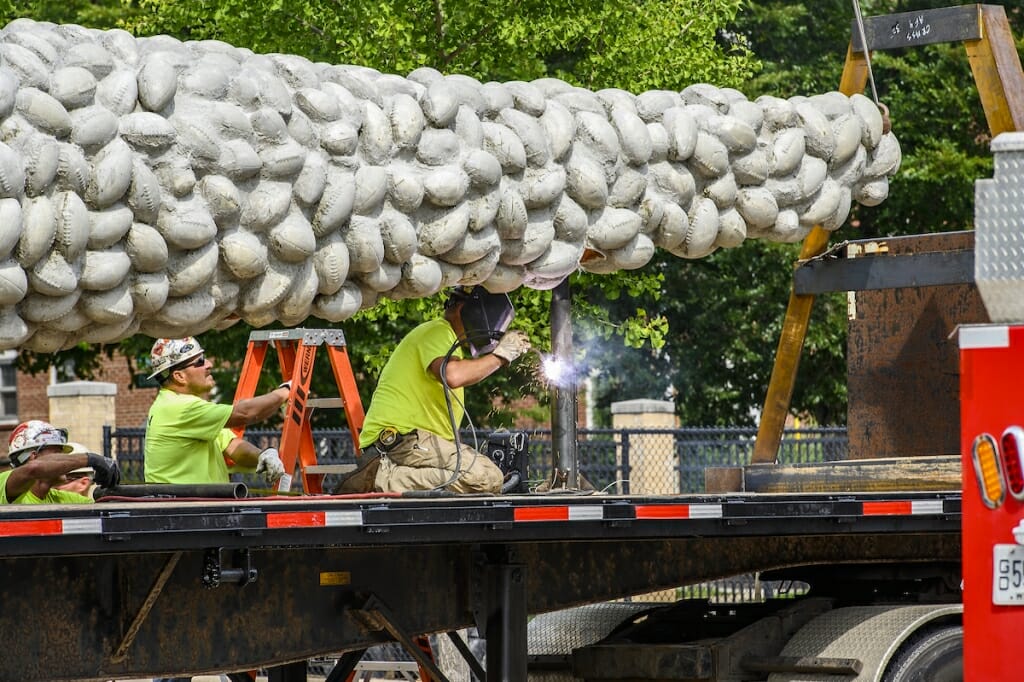 Photo: A worker welds a metal bar below the sculpture.