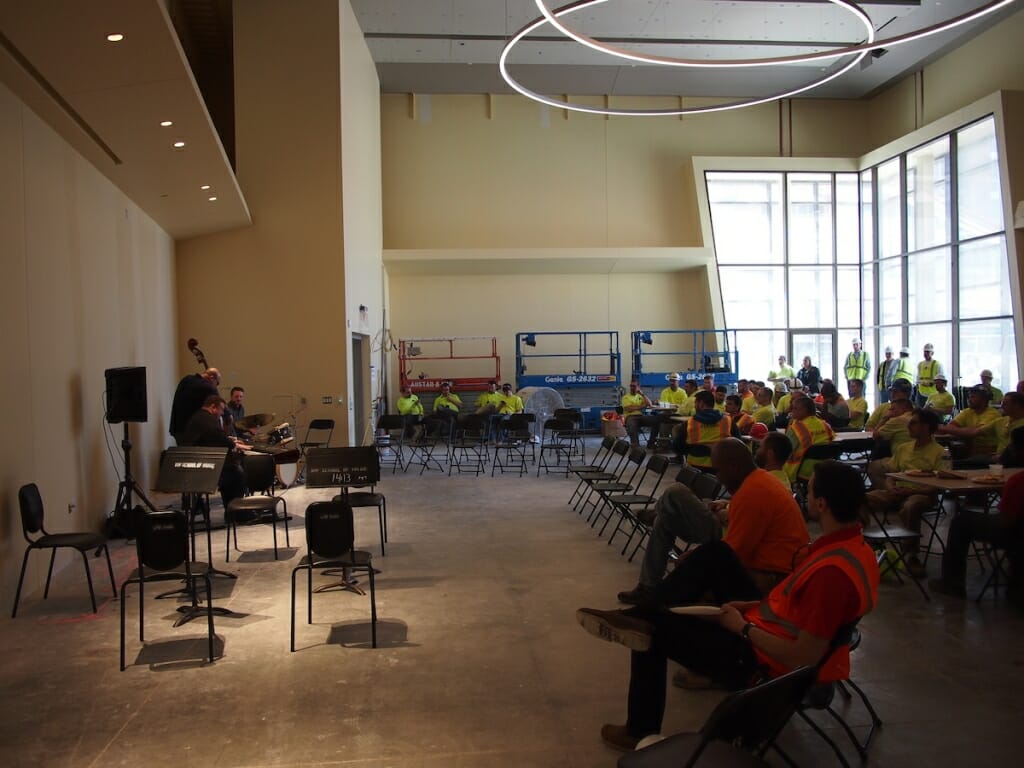 Photo: Construction workers listen in a partially built music hall to a string quartet.