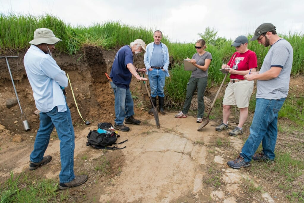 Photo: Fred digging into the ground surrounded by teachers and students