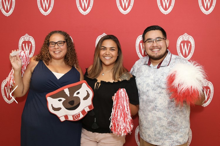 Photo of alumni holding red and white pom poms and a Bucky Badger cutout.